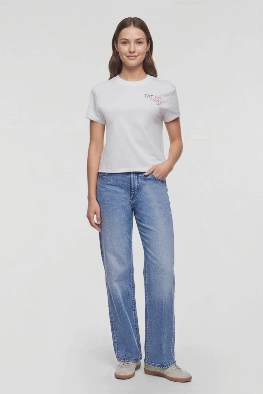 Video of a a woman modeling a white short-sleeve crewneck t-shirt with a small colorful graphic on the left chest that reads 'GET YOUR MAHJ ON', paired with blue jeans, against a plain white background. #color_snow-white