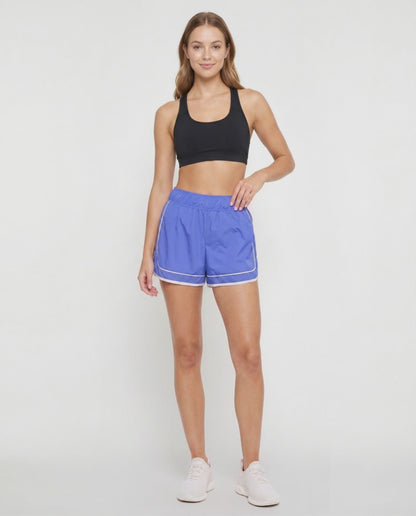 Video view of royal blue athletic shorts with white trim worn by a woman on a white background. 