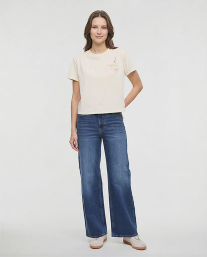 Video view of woman wearing a pale yellow t-shirt with a small chest embroidered design of spaghetti and a fork graphic on a white background. 