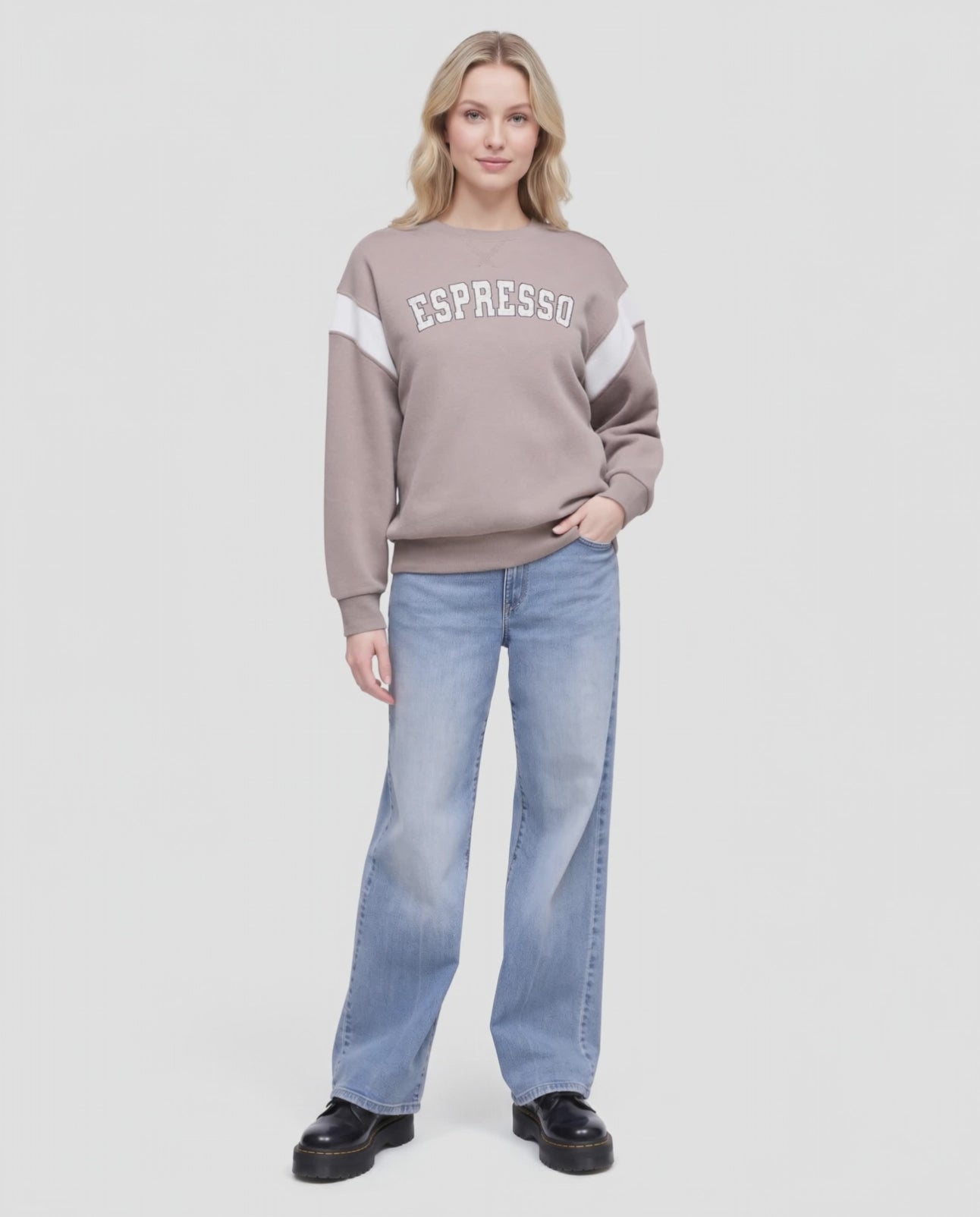 Video of A woman wearing a taupe crewneck sweatshirt with white color-blocked sleeves and 'ESPRESSO' printed in white arched letters on the chest, paired with light blue jeans, against a light gray background. #color_cinder