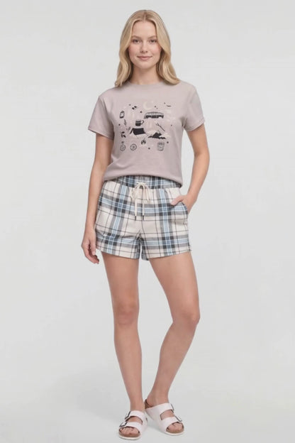 Video of a woman modeling a two-piece lounge set consisting of a light beige graphic t-shirt and matching plaid shorts in beige, blue, and white, paired with white slide sandals on a white studio background. 
