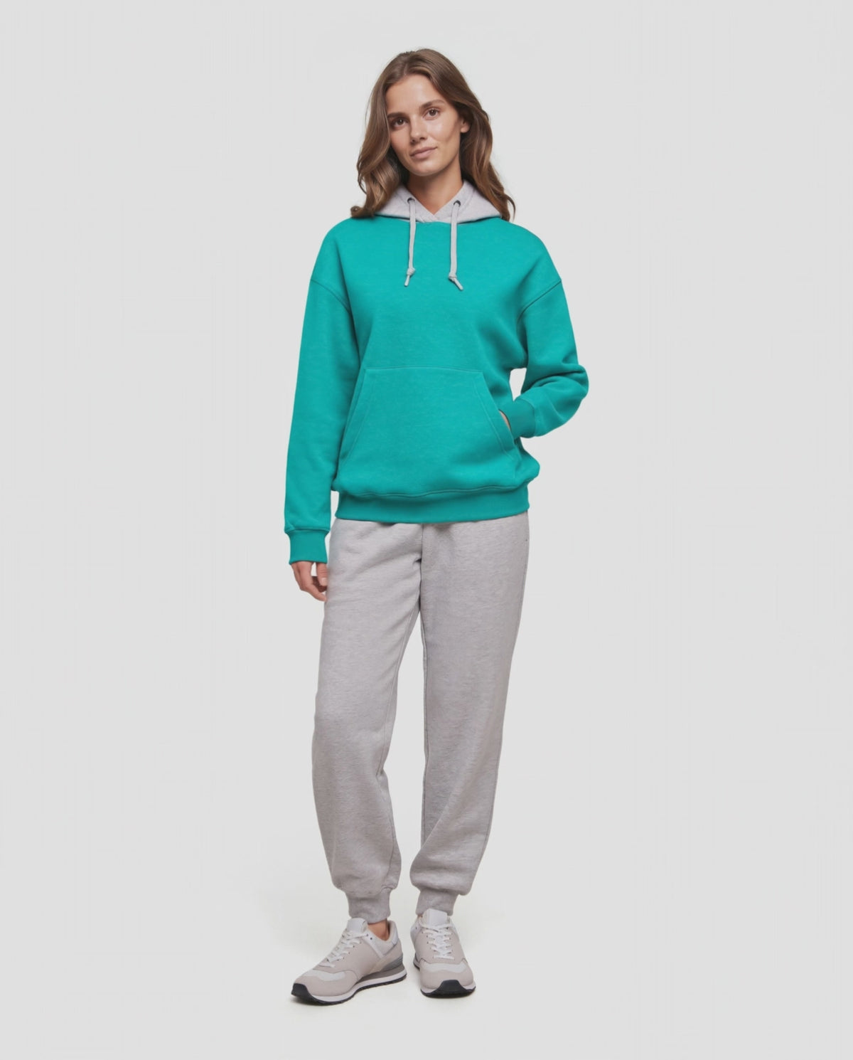 Video of A woman wearing a turquoise teal pullover hoodie with a light gray inner hood lining and white drawstrings, paired with light gray sweatpants, against a plain light gray background. 