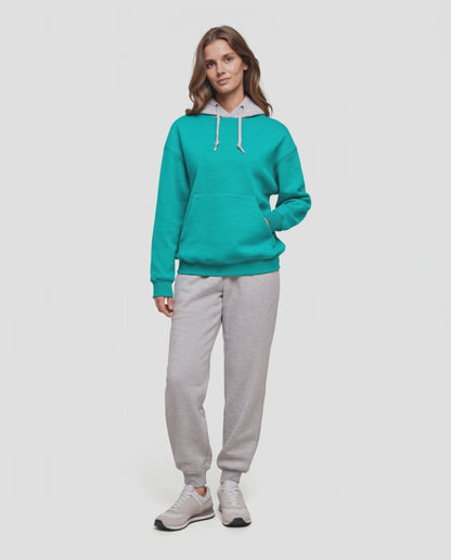Video of A woman wearing a turquoise teal pullover hoodie with a light gray inner hood lining and white drawstrings, paired with light gray sweatpants, against a plain light gray background. 