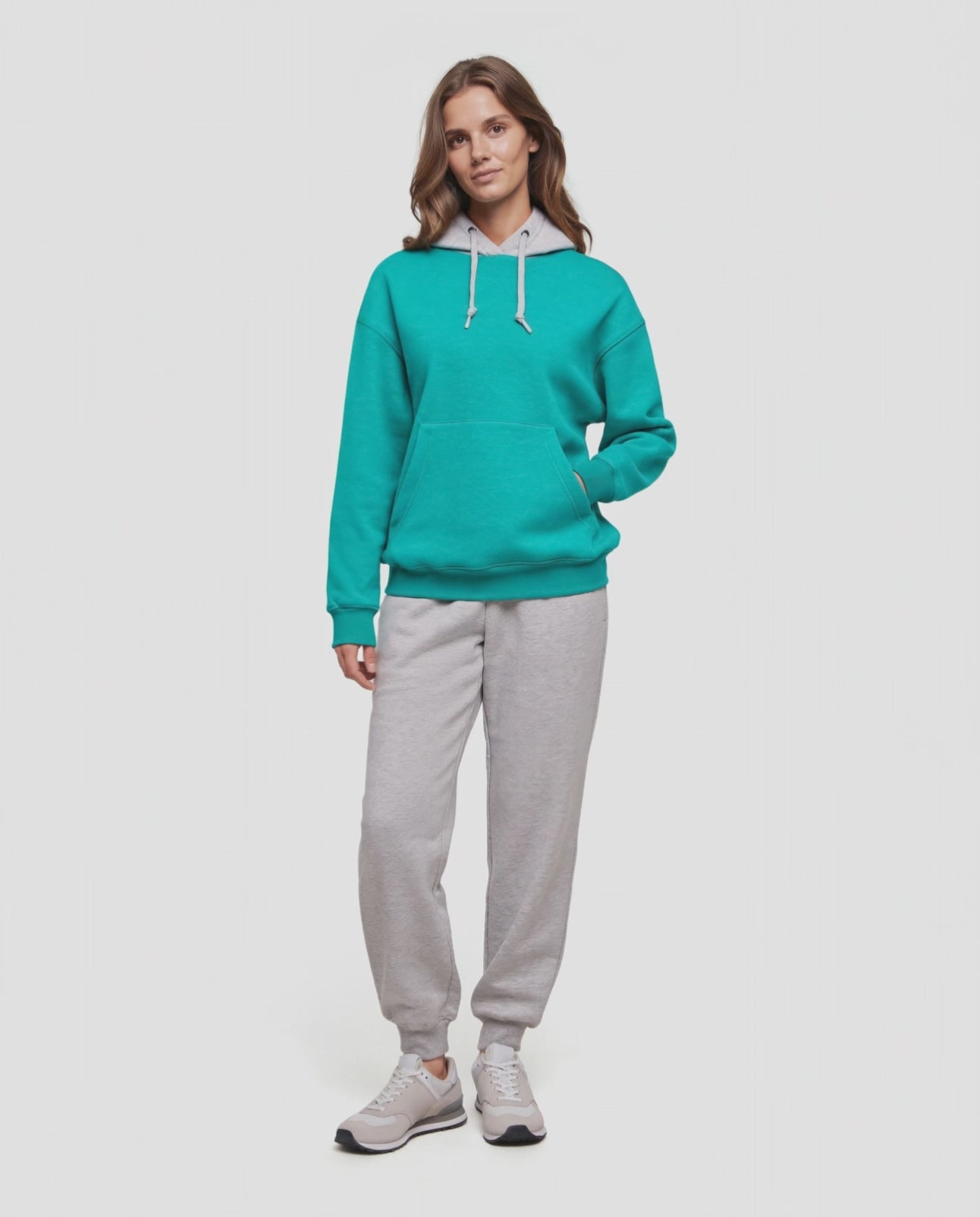 Video of A woman wearing a turquoise teal pullover hoodie with a light gray inner hood lining and white drawstrings, paired with light gray sweatpants, against a plain light gray background. #color_heather-paraleet