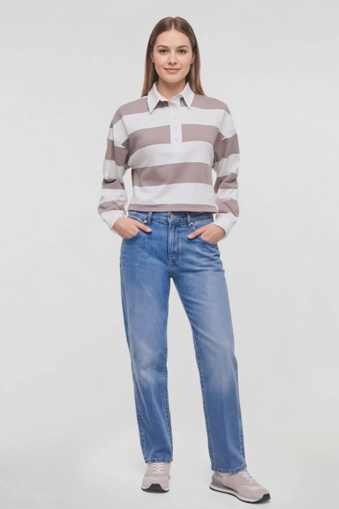 Video of a woman modeling a long-sleeve collared knit top with horizontal taupe and white stripes, paired with blue jeans and light gray sneakers, against a plain white studio background. 