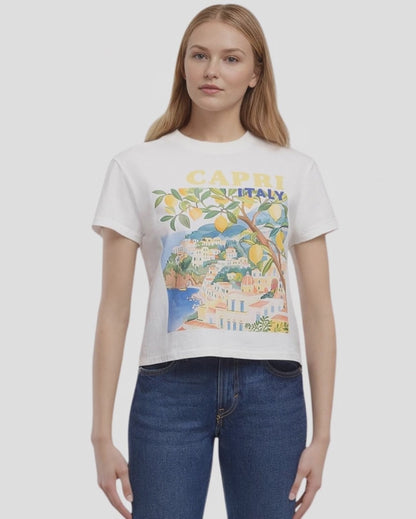 Video view of woman wearing a white t-shirt with a colorful graphic design of Capri, Italy, featuring buildings, trees, and lemons and &