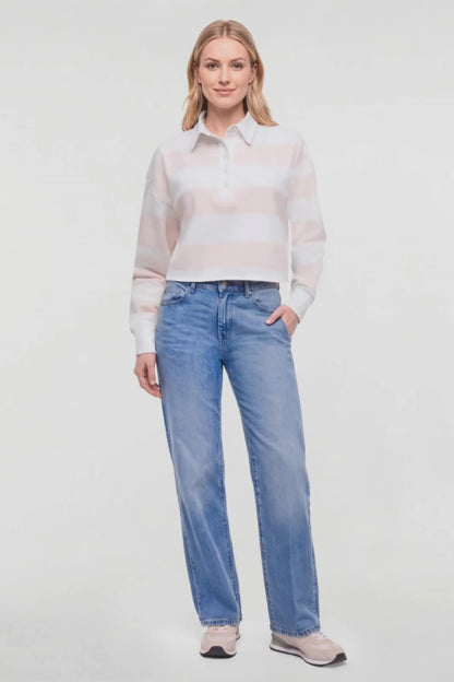 Video of A woman in wearing a crop light pink and white striped knit long-sleeve polo shirt, light-wash blue jeans, and pale pink sneakers, standing against a plain white studio background. 